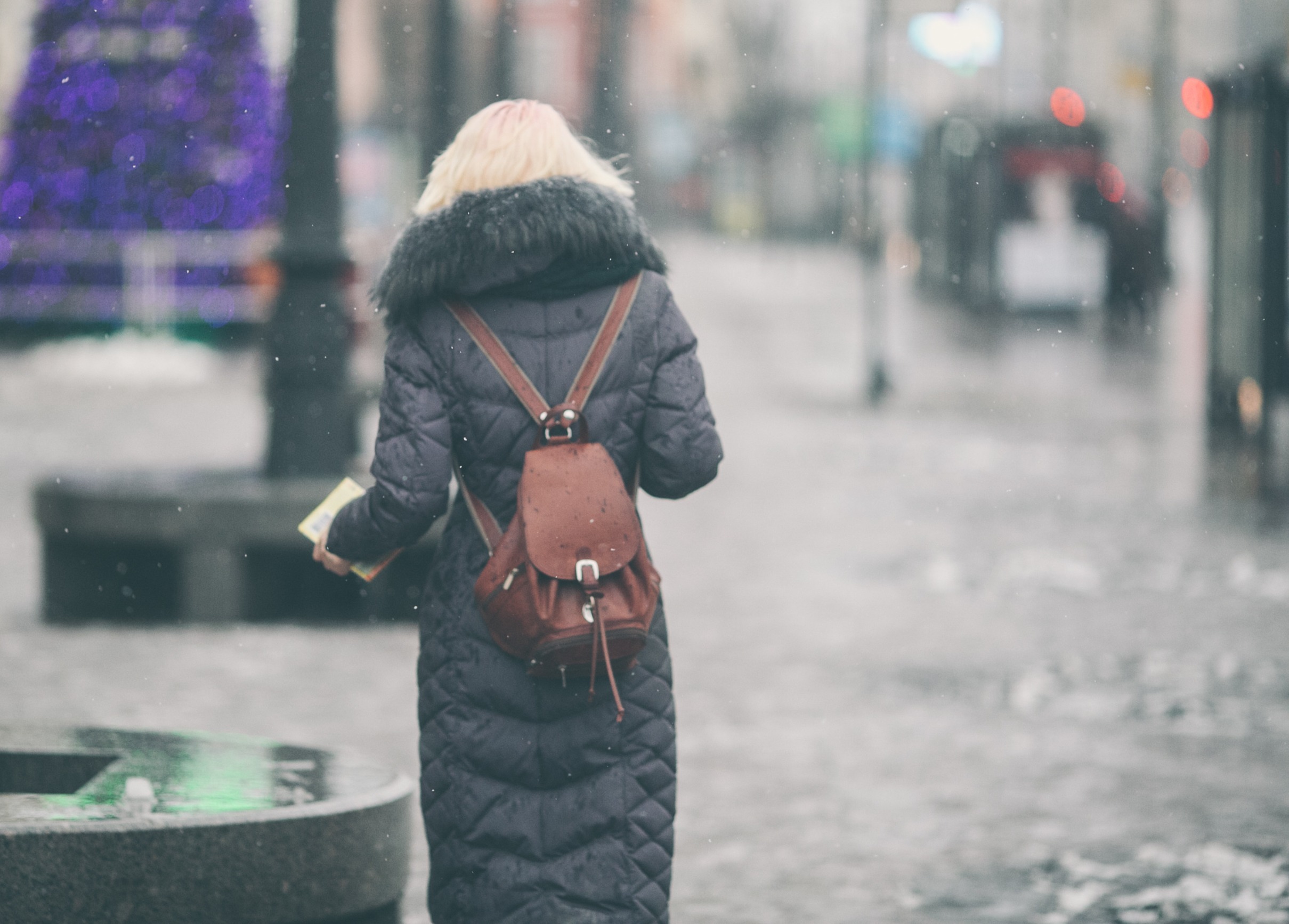 Photo d'une jeune femme vue de dos en Hiver se déplaçant dans la ville en pleine tempête de neige