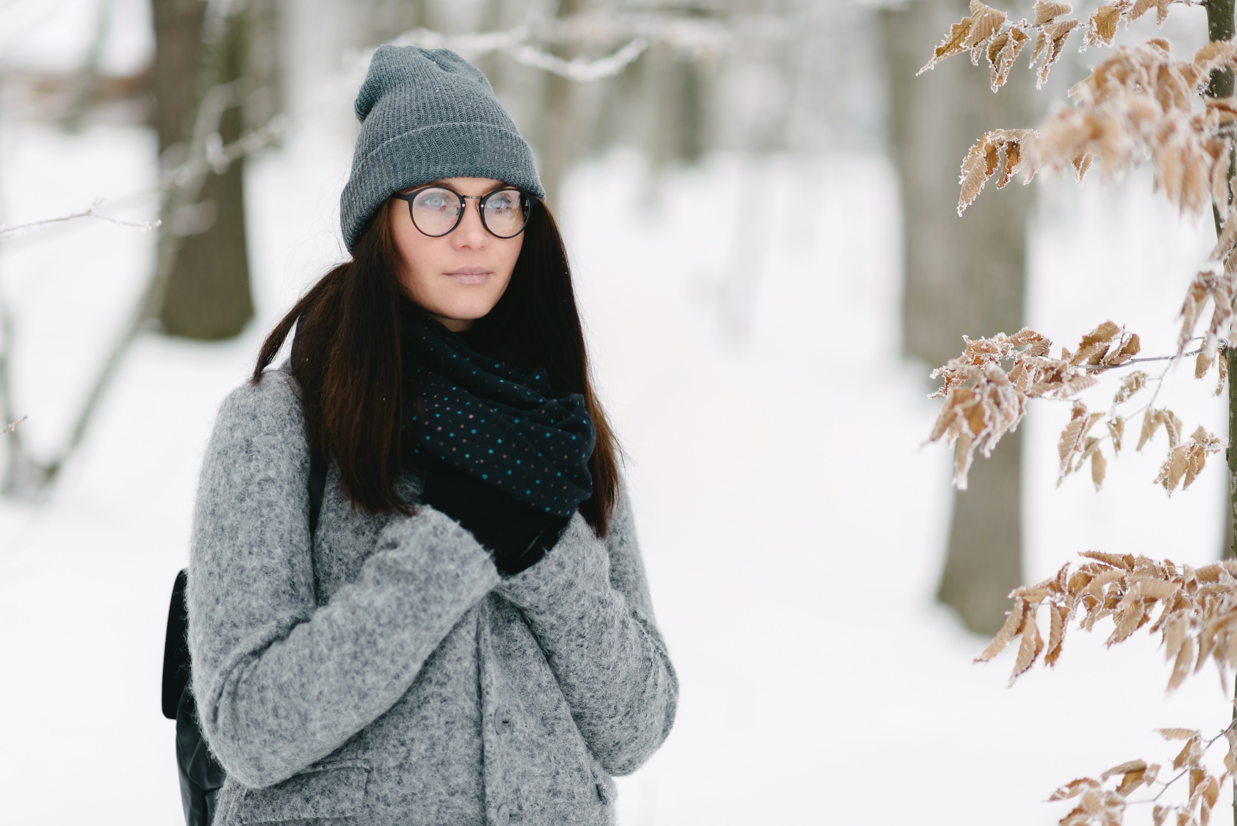 photo portrait d'une brune en manteau gris avec des lunettes et un sac à dos à l'extérieur dans la neige
