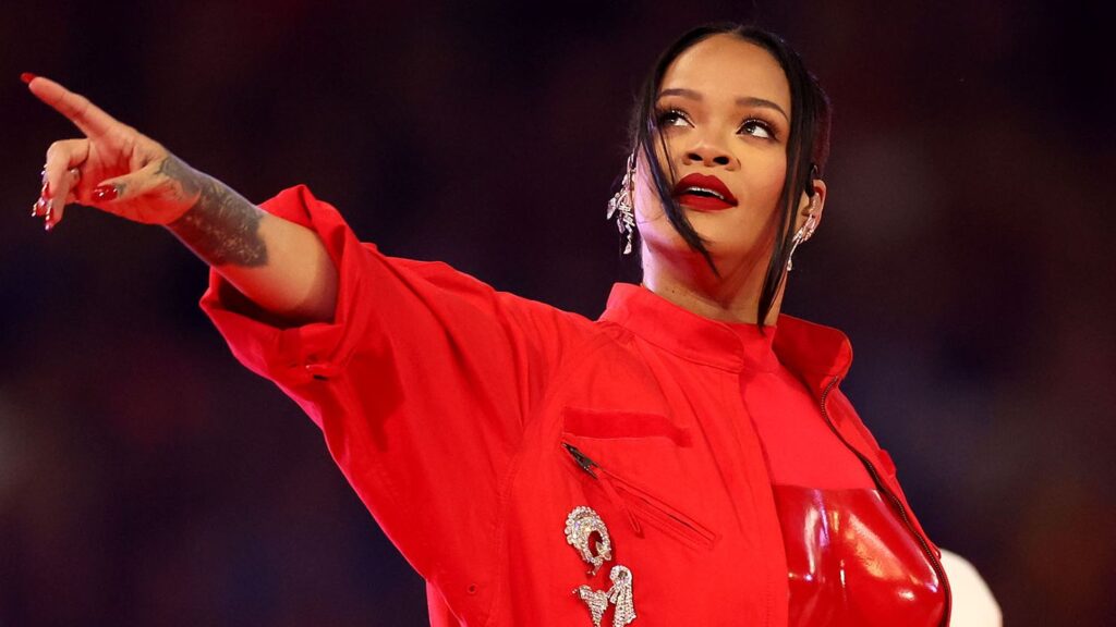 Photo de Rihanna au super bowl 2023, habillée en rouge et montrant du doigt son public