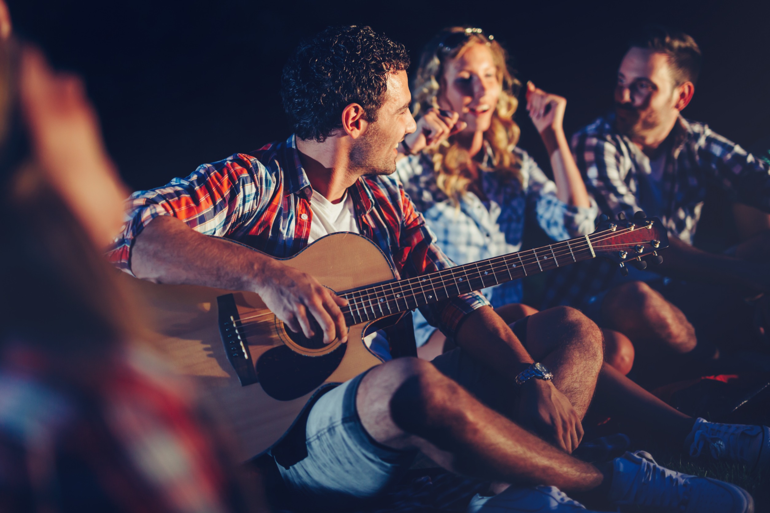 Des adultes, sur la plage, la nuit, entrain de chanter avec une guitare