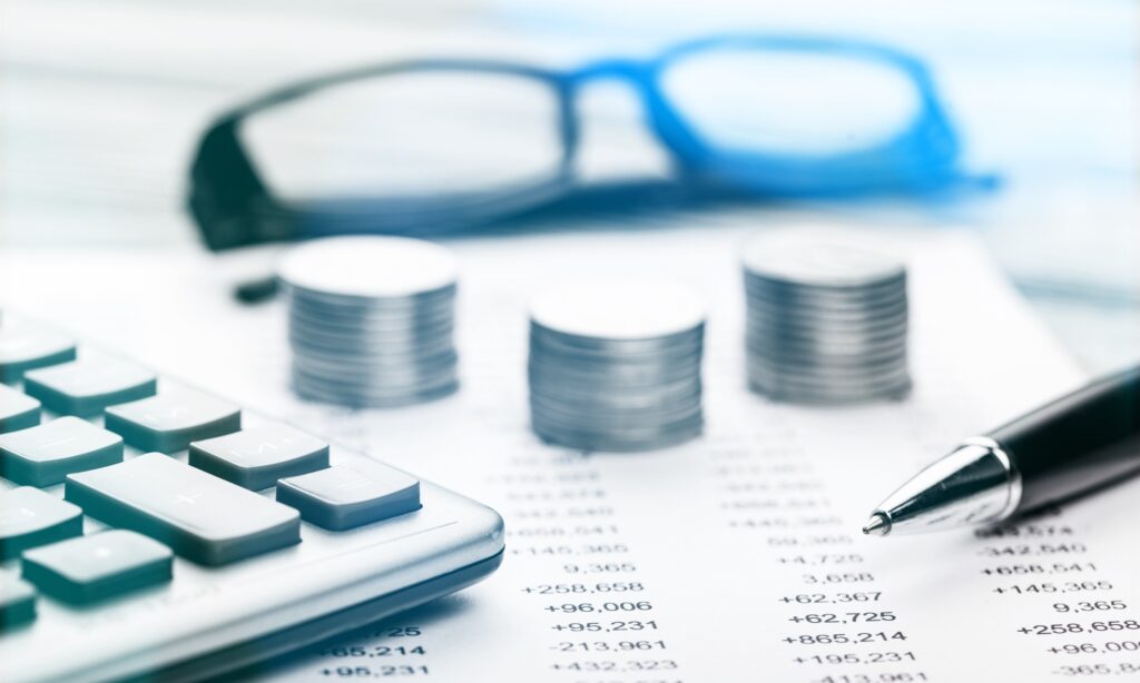 Photo gros plan de pièces de monnaies posées sur un document comptable avec une calculatrice et en fond des lunettes