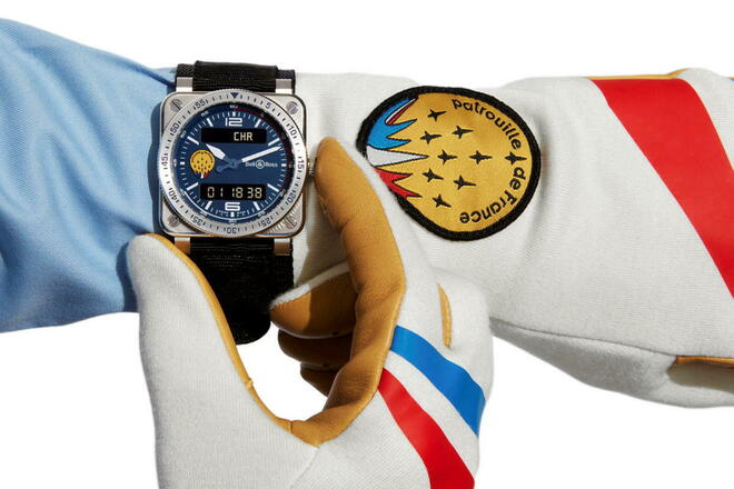 Une montre patrouille de france au bras d'un aviateur qui, la main dans son gant, règle sa montre.