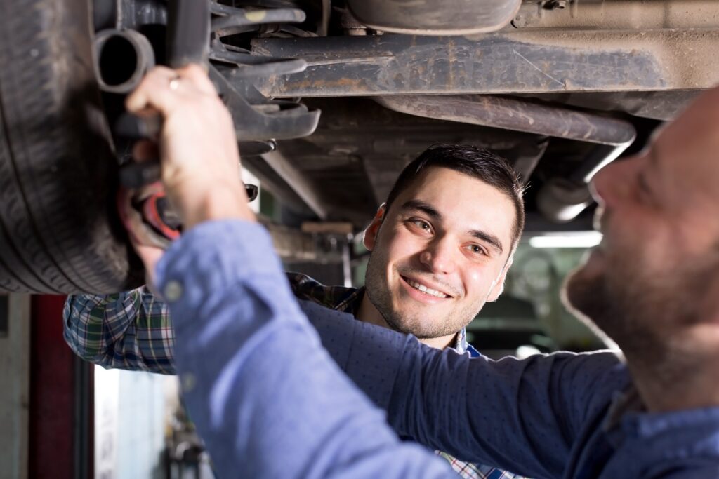 Un mecanicien à domicile, souriant avec son client, faisant une intervention sous le véhicule