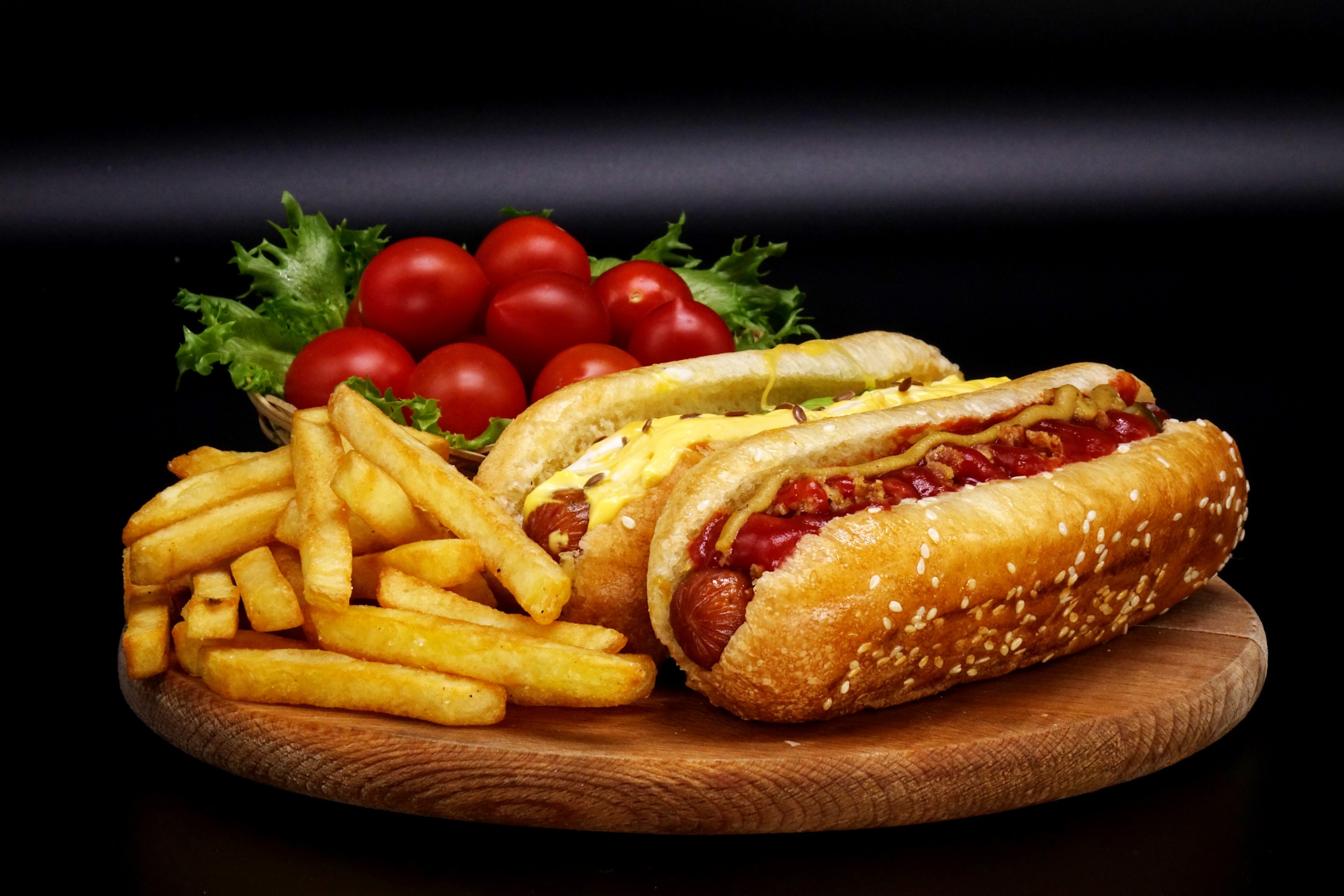 Hot-dogs, frites et saucisses à la sauce tomate et cerises sur une planche en bois.