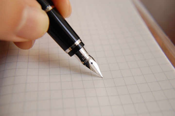 Une main tient un stylo plume et commence à rédiger une lettre sur un papier à carreaux