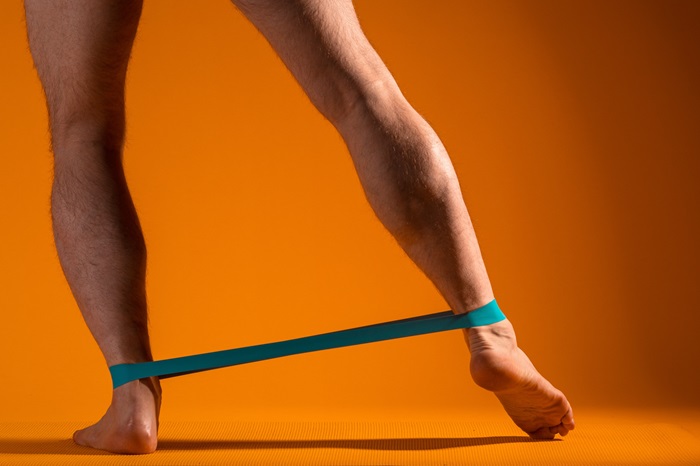 Un homme fait des exercices avec une bande élastiques pour entrainer ses jambes. Concept de muscle jambe