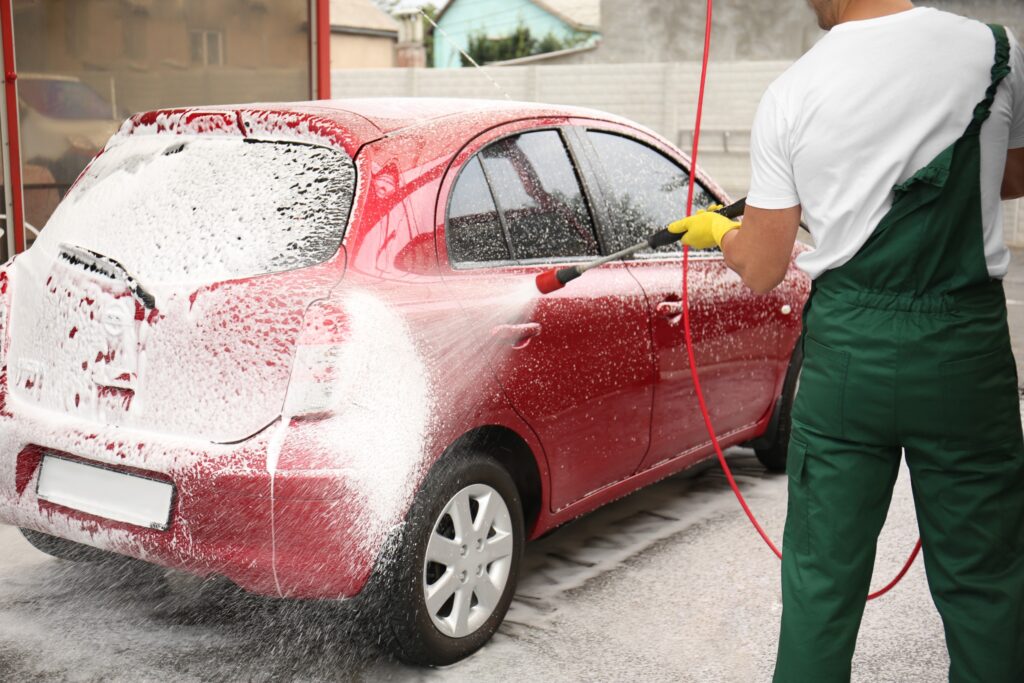 Une voiture entrain d'être nettoyé par un homme, avec un matériel de nettoyage à haute pression