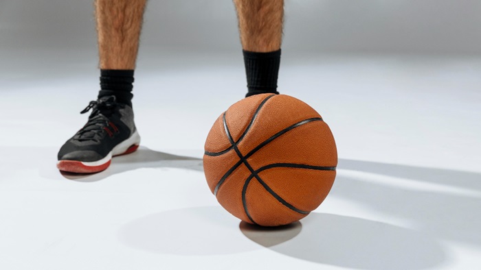 Zoom sur un ballon de basket sur un terrain de basket et en arrière plan les pied d'un basketteur