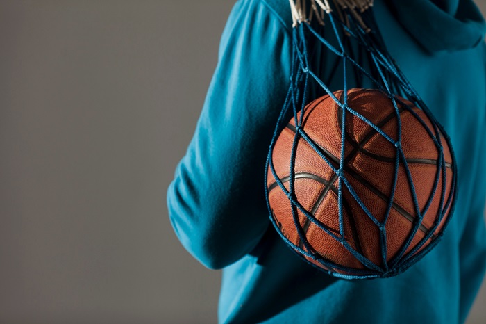 un ballon de basket dans un fillet sur l'épaule d'un jeune homme vu de dos