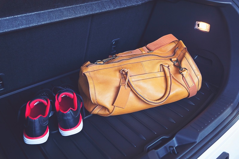 un sac de sport haut de gamme dans le coffre d'une voiture avec à coté des baskets noir et rouge