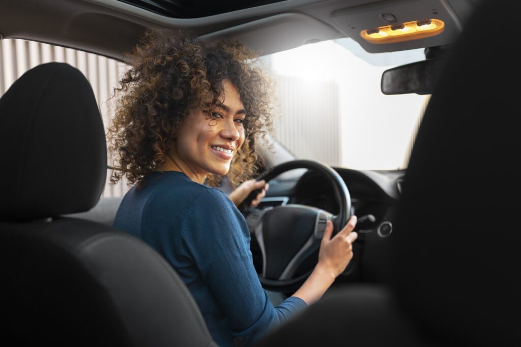 Une femme au volant d'une voiture de location pas cher est souriante au volant