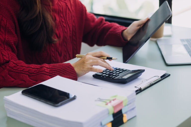 Femme, faisant un bilan comptable avec une pile de documents, une calculatrice et une tablette