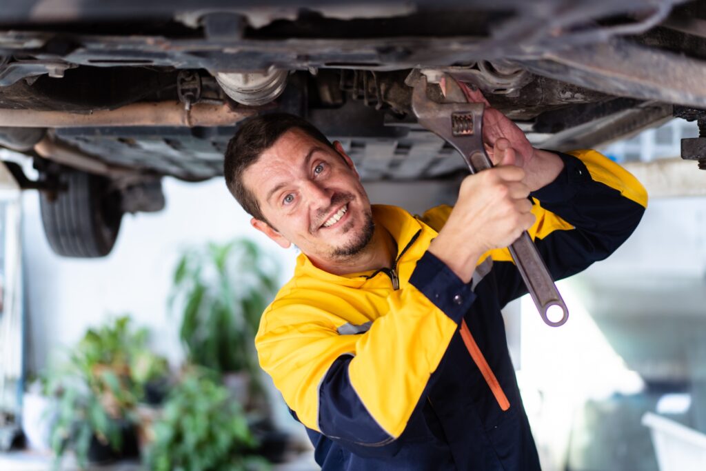 Un mécanicien souriant, sous la voiture surélevé, faisant une intervention à domicile