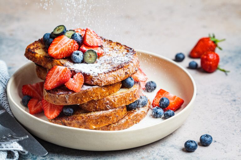 Pain perdu traditionnel aux myrtilles, avec de la fraises et du sucre en poudre. Met placée sur une assiette de couleur blanche