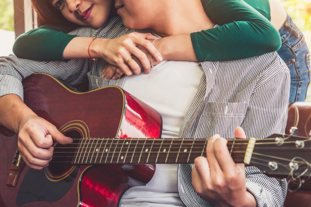Un couple amoureux passe un bon moment en écoutant une chanson d'amour. L'homme assis tenant une guitare et la femme entourant de ses mains, le cou de son chéri
