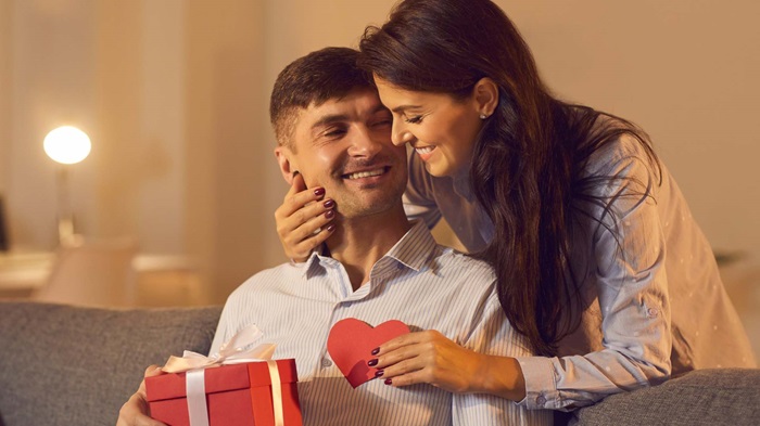 Un homme heureux reçoit un cadeau de saint valentin des mains de sa femme qui lui souris tendrement
